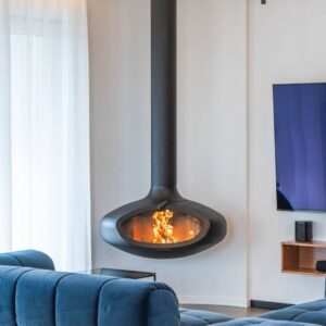 Suspended FireBob wood-burning fireplace in a contemporary living room with a blue sofa. The handcrafted circular fireplace hangs from the ceiling, creating a striking focal point while adding warmth and a calm, modern aesthetic to the space.